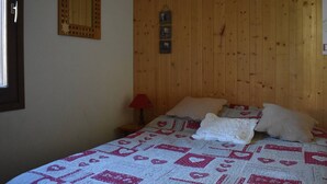 Een slaapkamer met een houten hoofdbord, een bed met een quilt met patroon, een nachtkastje met een lamp en een spiegel aan de muur.