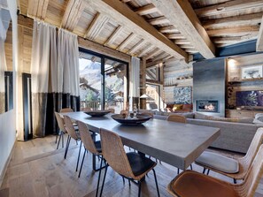 A dining area with a long table, wicker chairs, and a fireplace.