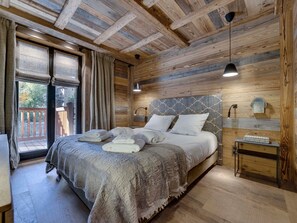 Quarto com painéis de madeira, uma cama, mesa de cabeceira, abajur e vista para o exterior.