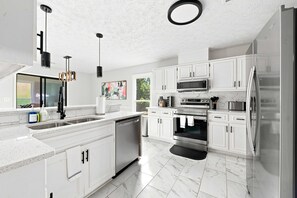 A modern kitchen with white cabinetry, stainless steel appliances, and a large island. - Flat Rock Stay w/ Game Room Near Fort Moore (Columbus)
