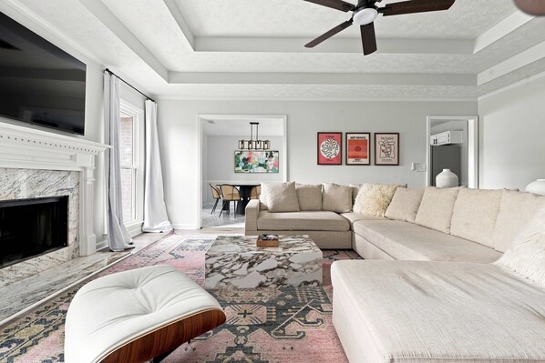 A modern living room with a fireplace, a ceiling fan, a sectional sofa, and a coffee table. - Flat Rock Stay w/ Game Room Near Fort Moore (Columbus)