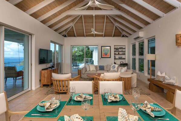 A spacious living area with a high ceiling, a dining table set for four, and a comfortable seating arrangement.