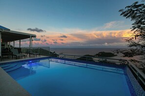 Ein Schwimmbecken mit Meerblick und einer überdachten Sitzgelegenheit.