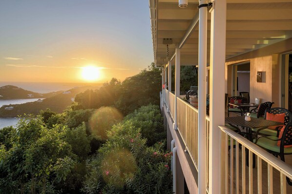 Un balcon offrant une vue imprenable sur le coucher de soleil sur l’océan, entouré d’une végétation luxuriante.