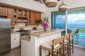 A kitchen with wooden cabinets, a stainless steel refrigerator, a gas stove, and a bar area with wicker chairs.