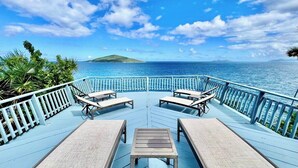 A deck with lounge chairs and a table overlooking a body of water with a distant island. - Oceanfront Villa-Private Pool-Panoramic Views -Sleeps 12 (St. Thomas)
