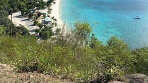 A coastal landscape with a sandy beach, clear turquoise waters, and lush green hills in the background. - Oceanfront Villa-Private Pool-Panoramic Views -Sleeps 12 (St. Thomas)