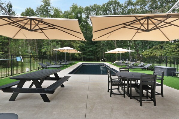 A poolside area with picnic tables and umbrellas, surrounded by a fence and greenery. - Harbor Country Farmhouse, Sleeps 26, Heated Pool, Hot Tub, Fire Pit (Three Oaks)