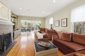 A modern living room with a fireplace, a sofa set, a dining area, and large windows.