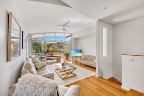A spacious living room with a large sliding glass door leading to a balcony, a ceiling fan, and a flat-screen TV.