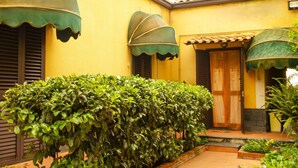 A yellow building with green awnings, a wooden door, and a well-maintained hedge.