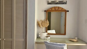 A bathroom with a white sink, a mirror, a wicker chair, and a closed wooden wardrobe.