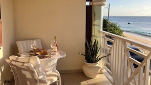 A balcony with a table set for two, a potted plant, and a view of the sea.