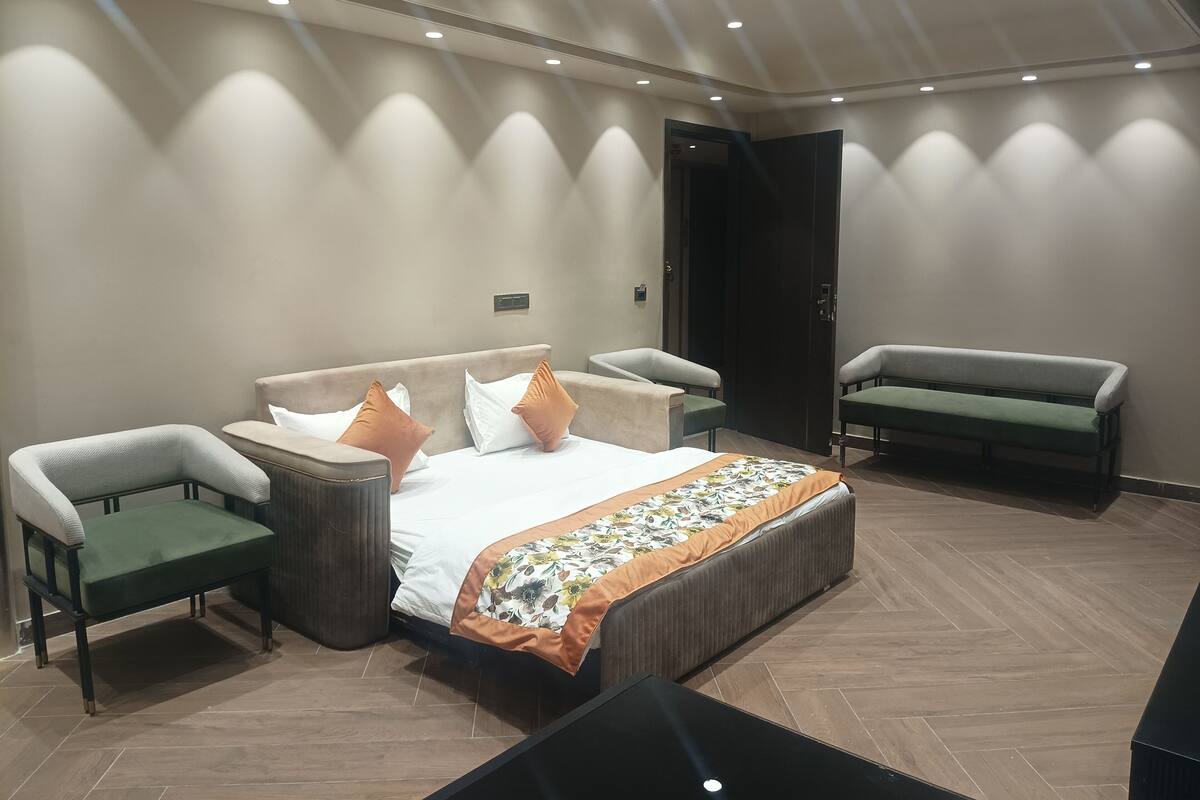 A modern hotel room with a bed, two armchairs, a bench, and a wooden floor.