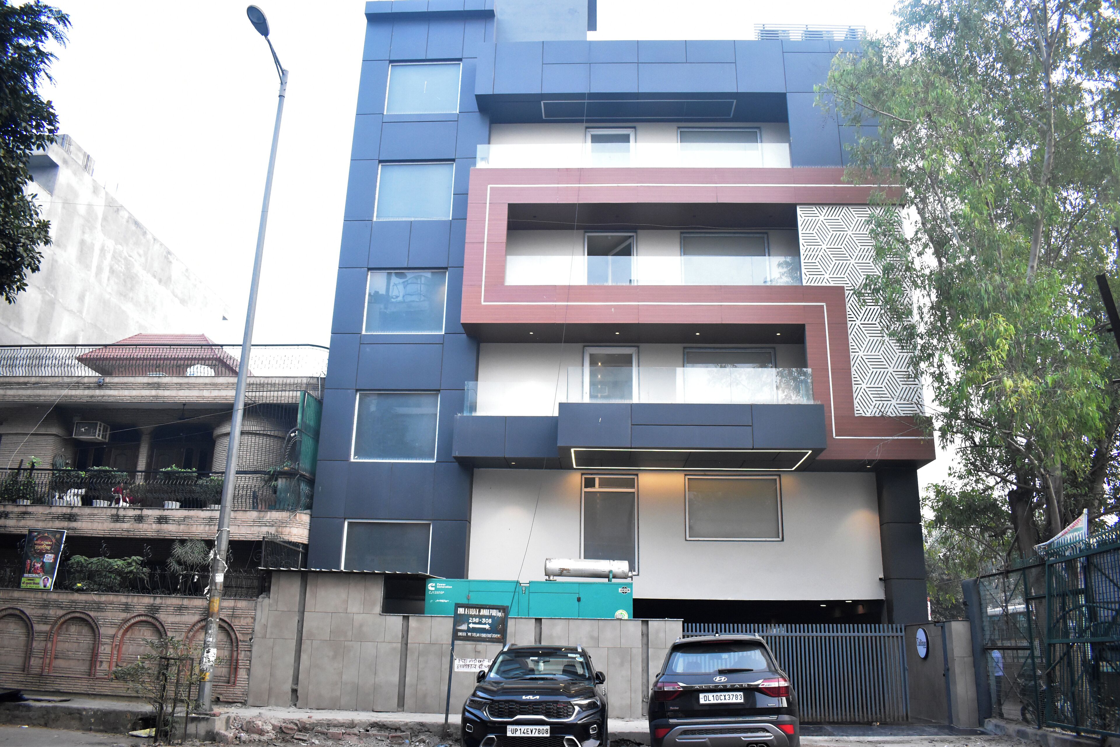 A multi-story building with a modern design, featuring a mix of rectangular and square windows, a patterned facade, and a gated entrance.