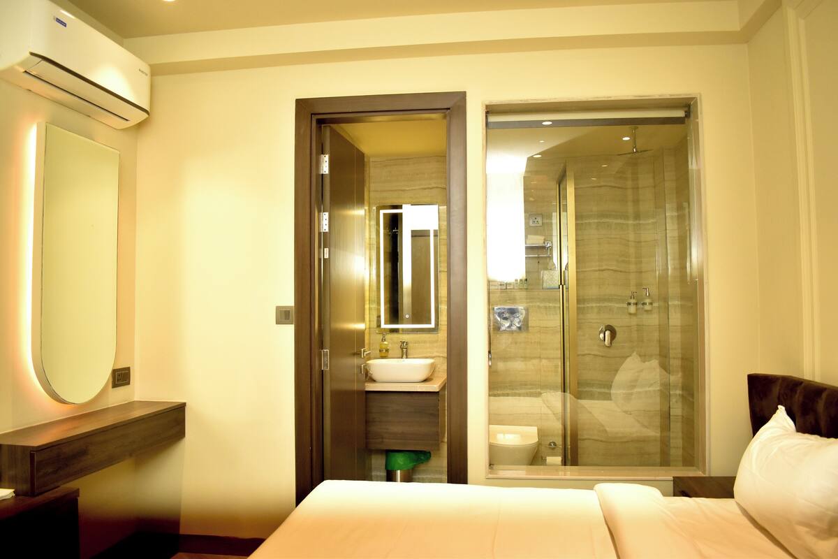 A hotel room with a bed, a bathroom with a glass shower, and a sink.