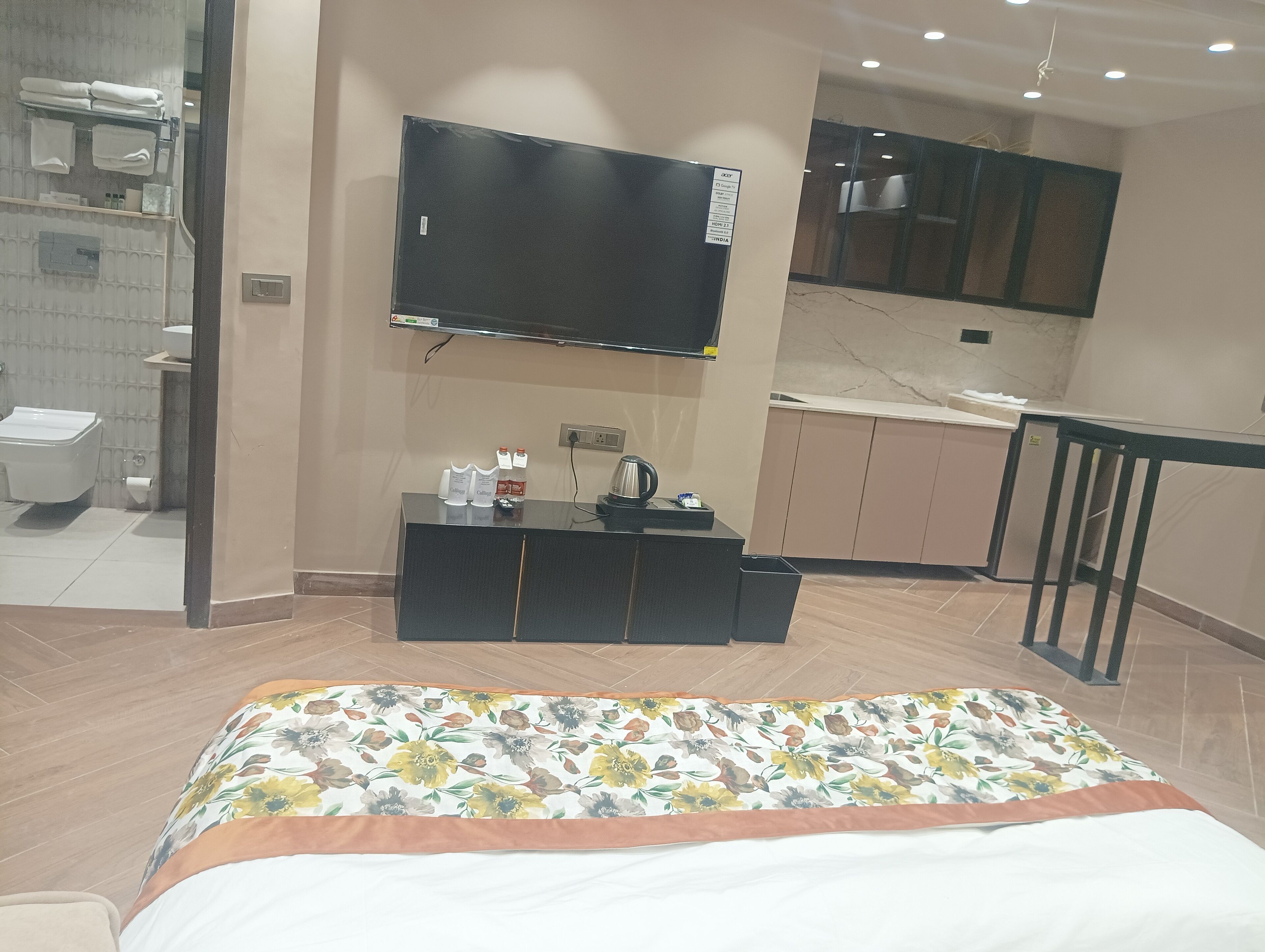 A hotel room with a bed, a desk with a flat-screen TV, a bathroom with a toilet and sink, and a kitchenette with cabinets and a countertop.