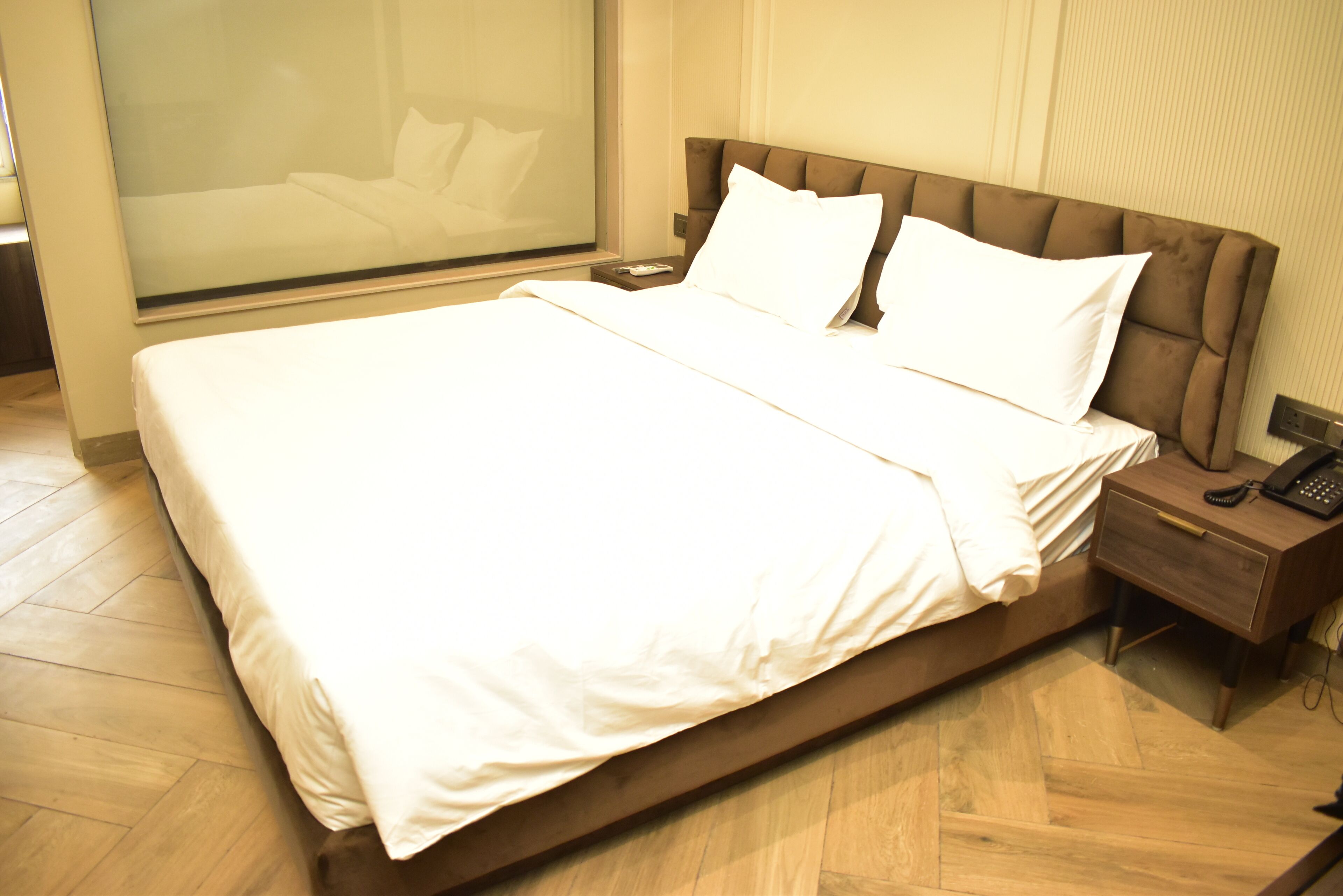 Un grand lit avec du linge de lit blanc, une tête de lit en bois et une table de chevet avec un téléphone.