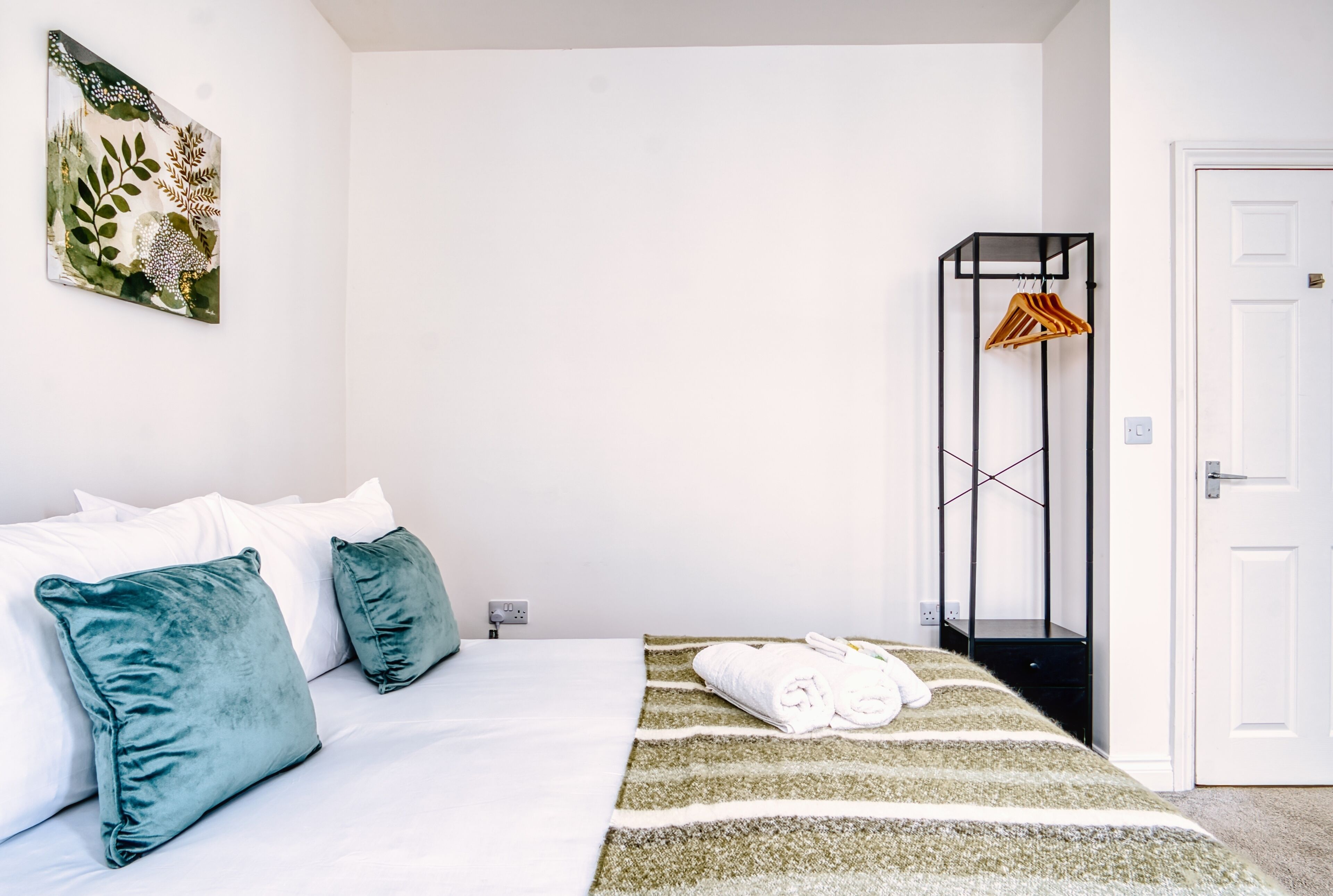 A hotel room with a bed, pillows, a striped rug, a towel, and a hanging rack.