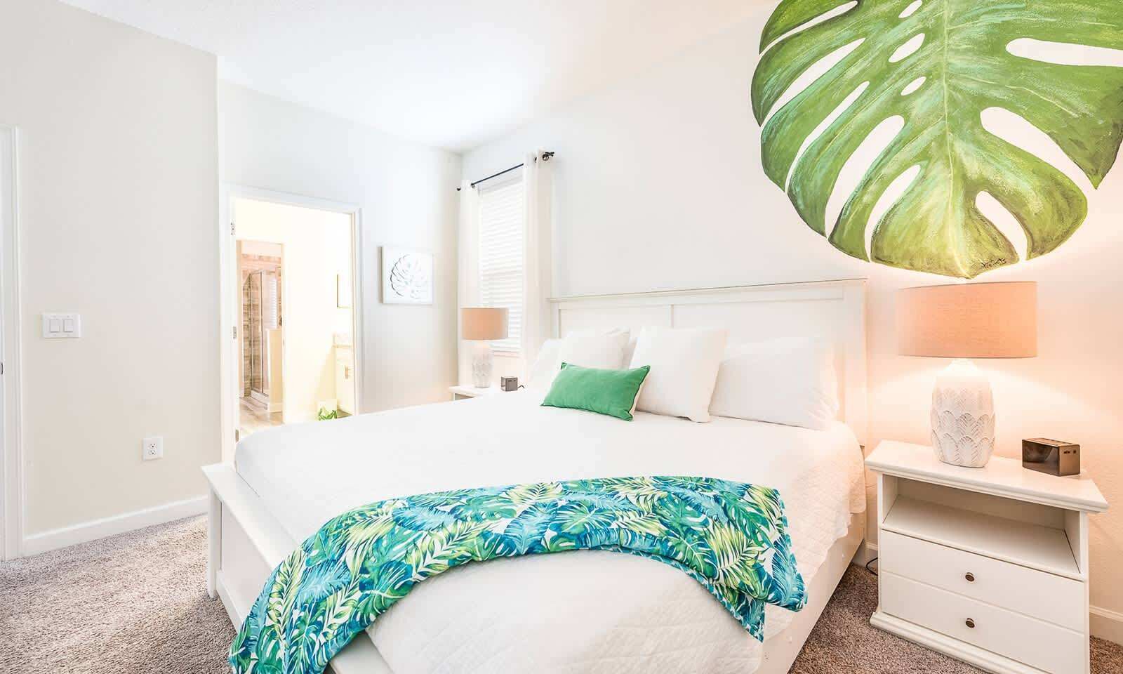 Une chambre à coucher avec un lit, une table de chevet, une lampe et une grande décoration représentant une feuille tropicale.