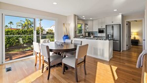 A modern kitchen with a central island, built-in appliances, and a dining area with a large window overlooking a garden. - Oceanview Townhome Steps from Iconic Windansea Beach (San Diego)