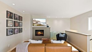 A modern living room with a fireplace, a sofa set, and framed artwork on the walls. - Oceanview Townhome Steps from Iconic Windansea Beach (San Diego)