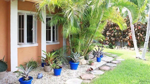 Une maison dotée d’un porche abrité, de plantes en pot et d’un chemin en pierre.