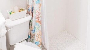 Une salle de bain avec des toilettes, une poubelle blanche et un rideau de douche à motifs corail.