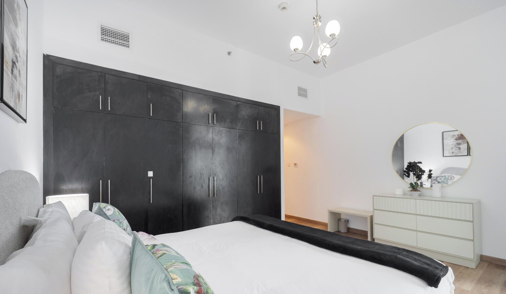 A bedroom with a large bed, a wardrobe, a bedside table, a mirror, and a chandelier.