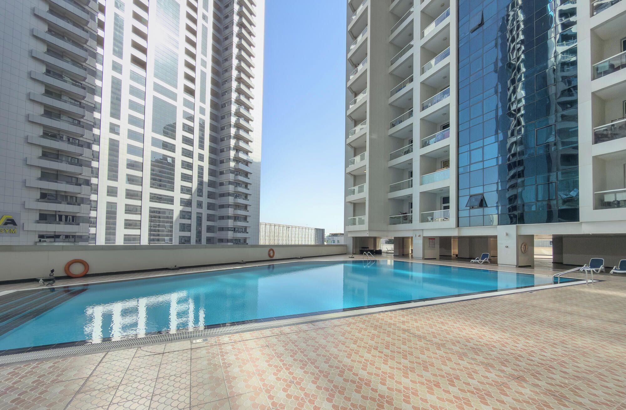 A swimming pool with a tiled deck, surrounded by high-rise residential buildings.