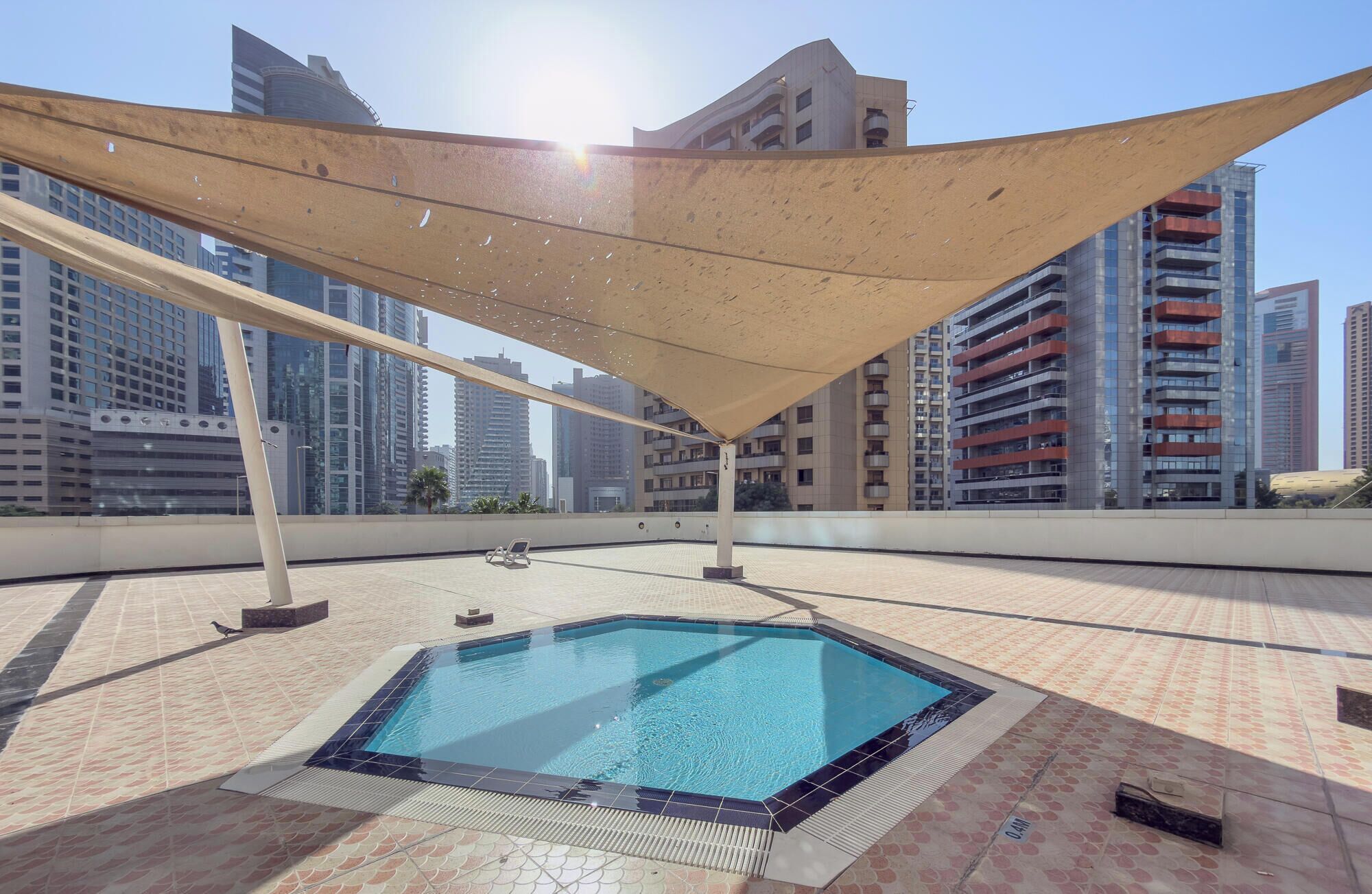 Una piscina en la azotea con toldo, rodeada de edificios altos.