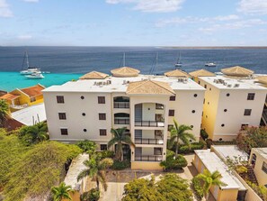 Un hôtel situé sur la côte, doté de nombreux balcons, d’un espace piscine et offrant une vue sur la mer et les bateaux.