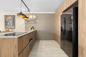 Une cuisine moderne avec des meubles en bois, un réfrigérateur noir et des luminaires suspendus.