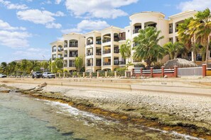 A beachfront hotel with multiple balconies, palm trees, and a rocky shoreline. - Elegancia Ocean View with Cooling Pool (Kralendijk)