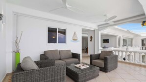 Un vaste espace de vie agrémenté de meubles en osier, d’un ventilateur de plafond et offrant une vue sur le balcon extérieur.