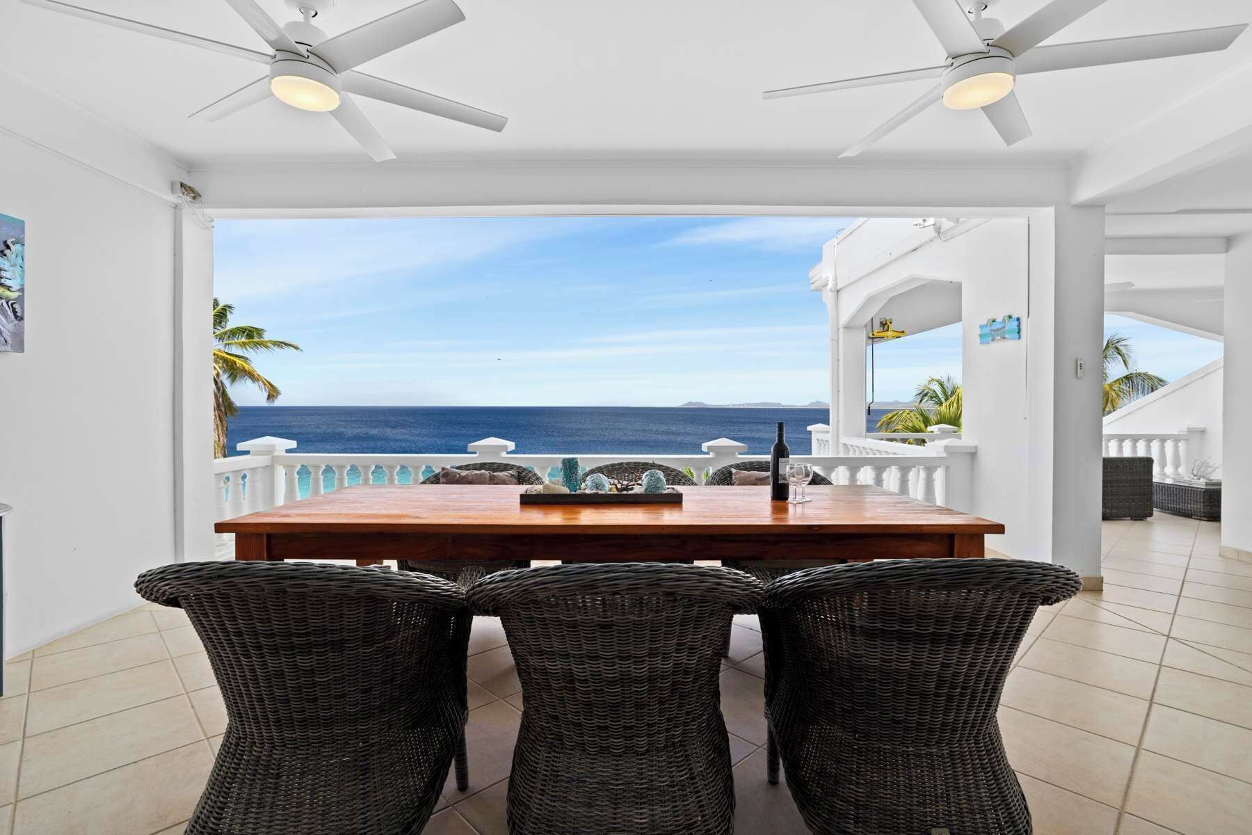 Un espace repas comprenant une table et des chaises, un ventilateur de plafond et une vue sur l’océan.