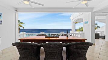 Un espace repas comprenant une table et des chaises, un ventilateur de plafond et une vue sur l’océan.