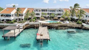 Un complexe hôtelier comprenant plusieurs bâtiments, une jetée en bois et une piscine à l’eau cristalline.