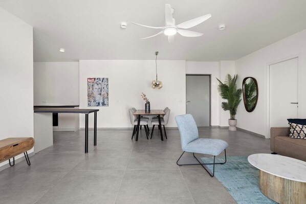 A modern living room with a dining area, a ceiling fan, a potted plant, and a wall-mounted mirror.