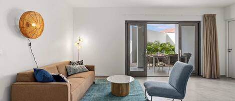 A modern living room with a sofa, a coffee table, and a chair. There is a ceiling fan, a wall-mounted light, and a sliding glass door leading to an outdoor area with a table and chairs.