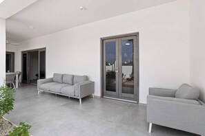 A modern outdoor living area with a grey sofa, a dining table with chairs, and a sliding glass door.