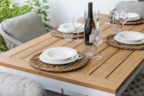 Une table de salle à manger en bois, dressée avec de l’assiette blanche, des verres transparents et une bouteille de champagne.