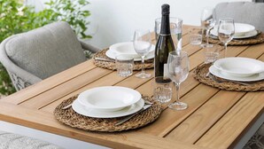 A wooden dining table set with white plates, clear glasses, and a bottle of champagne. - Bonaire Beach Apartments 2 with a palm garden, a refreshing shared pool and a private sitting area (Kralendijk)