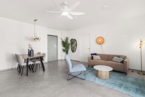 Una sala de estar moderna con comedor, ventilador de techo, lámpara de pared y sofá con cojines.