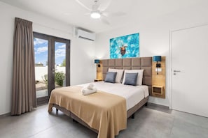 A hotel room with a bed, a ceiling fan, a painting of a sea turtle, and a view through the glass door. - Bonaire Beach Apartments 2, pool and palm garden (Kralendijk)