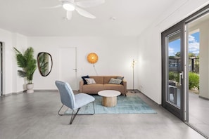 A modern living room with a sofa, a coffee table, a chair, a ceiling fan, a floor lamp, and a large window with a view of the outdoors.
