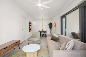 A modern living room with a ceiling fan, a dining area with a table and chairs, a sofa with cushions, and a large window.