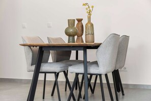 A dining table with four grey upholstered chairs and a wooden top. There are three vases on the table, one of which has yellow flowers.