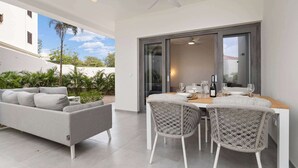A modern outdoor dining area with a table and chairs, a sofa, and a view of a building and greenery.