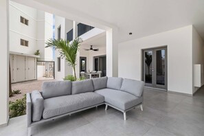 A modern living room with a grey sectional sofa, a dining area with a table and chairs, and a large sliding glass door.